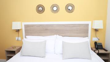 A hotel room with a large bed, two bedside tables, a wall-mounted phone, and three decorative mirrors.