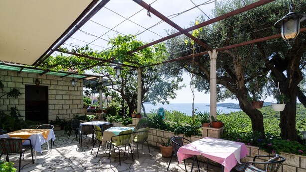 Eine Terrasse im Freien mit Steinboden, Tischen mit Tischdecken und Stühlen.
