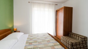 Ein Hotelzimmer mit einem Bett, einem Nachttisch mit Lampe, einem Fenster mit durchsichtigen Vorhängen, einem Holzschrank und einem Karo-Sofa.