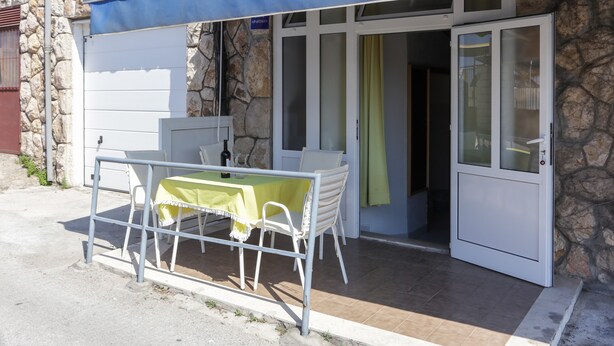 An outdoor seating area with a table and chairs, a stone wall, and a blue awning.