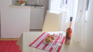 Eine kleine Küche mit weißen Schränken, einem Fenster mit durchsichtigen Vorhängen und einem Essbereich mit Tisch für zwei Personen.