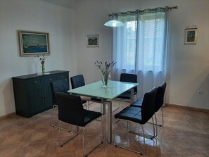 Un coin repas comprenant une table en verre, quatre chaises noires, un buffet en bois foncé et deux tableaux encadrés accrochés aux murs.
