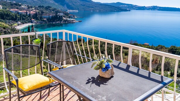 Un balcón con dos sillas y una mesa, con vistas a un lago y un paisaje montañoso.