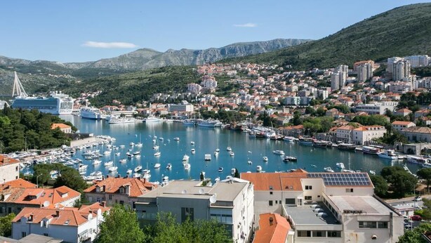 Uma vila costeira com um porto cheio de barcos, rodeada por edifícios residenciais e colinas.