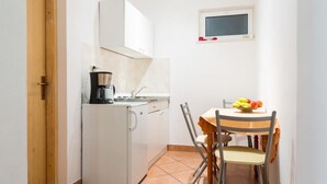 Una cocina compacta con refrigerador, cafetera y una pequeña mesa de comedor con sillas.