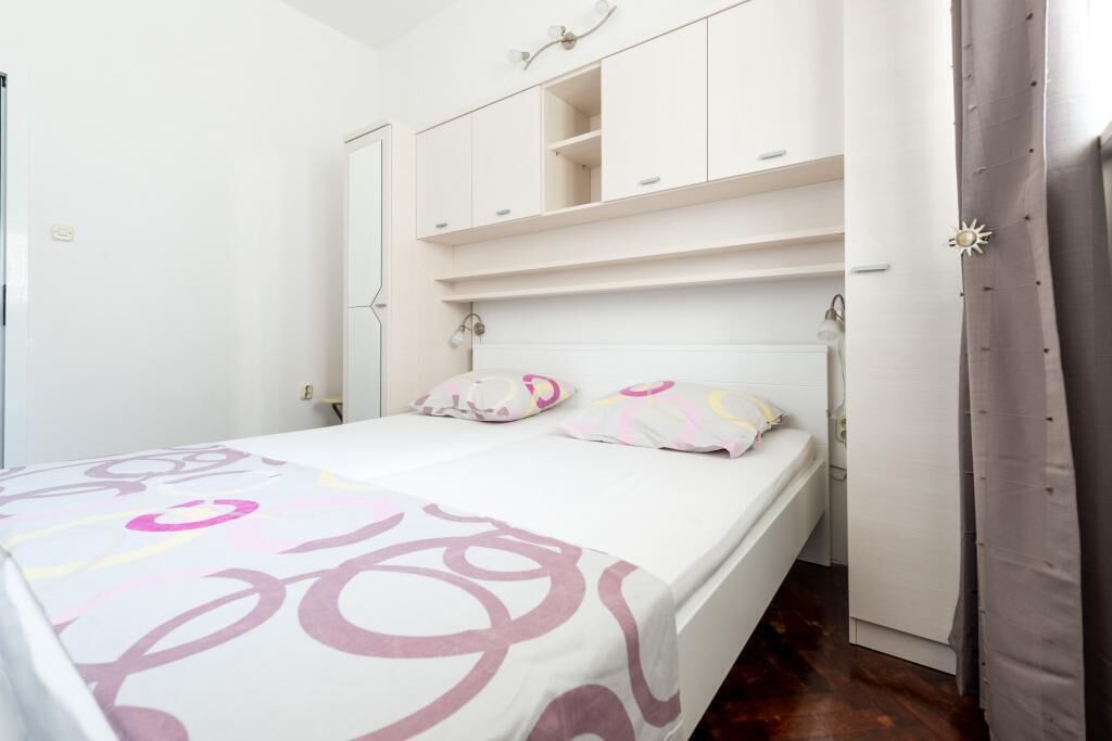 Un dormitorio con cama, paredes blancas, un armario y una cortina.