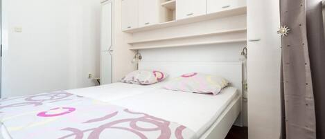 Un dormitorio con cama, paredes blancas, un armario y una cortina.