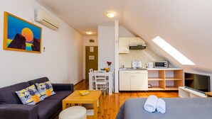 Ein kleines Zimmer mit Schlafgelegenheit, einer Couch, einem Esstisch, einer Küchenzeile und einem Fernseher.