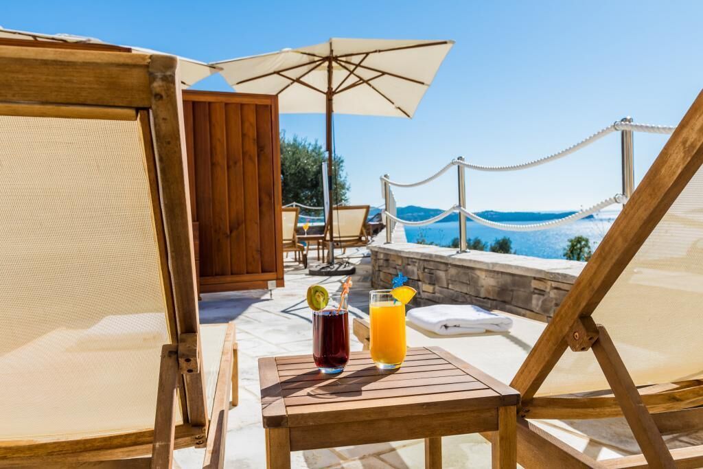 Una terraza de madera con una mesa, dos bebidas y vistas al mar.
