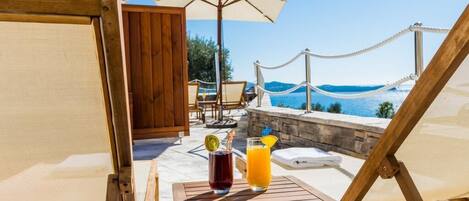 Una terraza de madera con una mesa, dos bebidas y vistas al mar.