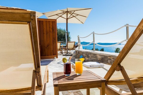 A wooden deck with a table, two drinks, and a view of the sea.