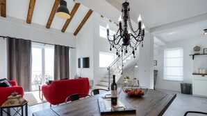 Un amplio salón con una mesa de comedor de madera, sillas rojas, una araña y una escalera que sube a un nivel superior.