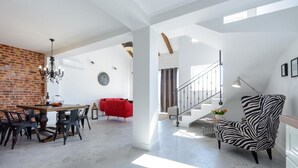 Amplia sala de estar con una mesa de comedor, sofá rojo, sillón estampado de cebra y una escalera que conduce a un nivel superior.