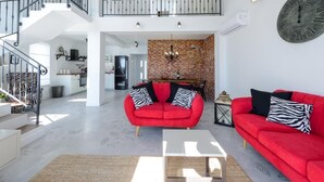 Un salón amplio con un sofá rojo, una mesa de centro blanca y un sofá rojo más. Se ve una escalera que sube a un nivel superior.