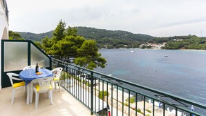 A balcony with a table and chairs, overlooking a body of water with boats and a hilly landscape in the distance. - Apartments Posta - Studio with Balcony and Sea View (Saplunara)