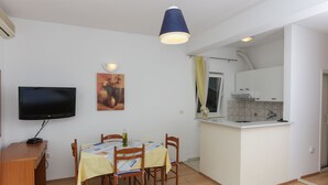 A compact living space with a dining area, kitchenette, and a TV mounted on the wall. - Apartments Posta - Studio with Balcony and Sea View (Saplunara)