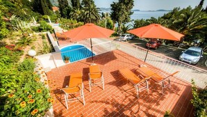 Un área de piscina en la azotea con sillas y sombrillas naranjas, rodeada de exuberante vegetación y vistas al mar.