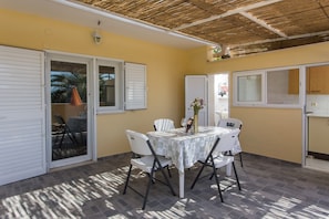 An outdoor patio with a table and chairs, a thatched roof, and a sliding glass door.