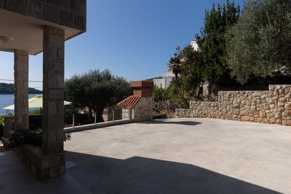 A stone building with a red-tiled roof, a paved area, and a view of the sea.