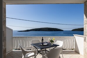A balcony with a table, chairs, and a view of the sea and a distant island.