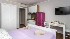 A hotel room with a bed, a desk, a TV, a wardrobe, and a kitchenette.