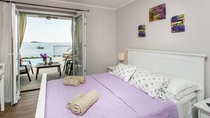 A bedroom with a bed, a view of the sea, and a balcony with a table and chairs.