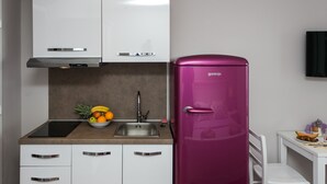 A modern kitchen with white cabinets, a stainless steel sink, and a purple refrigerator.