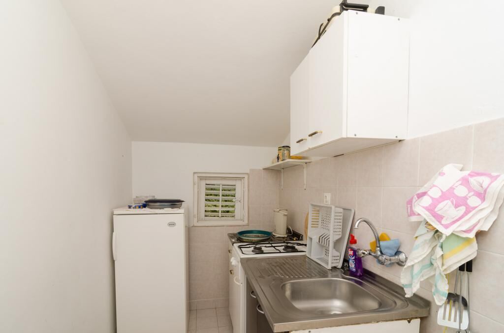 Une cuisine de taille réduite, équipée d’un réfrigérateur, d’une cuisinière, d’un évier et de meubles blancs.