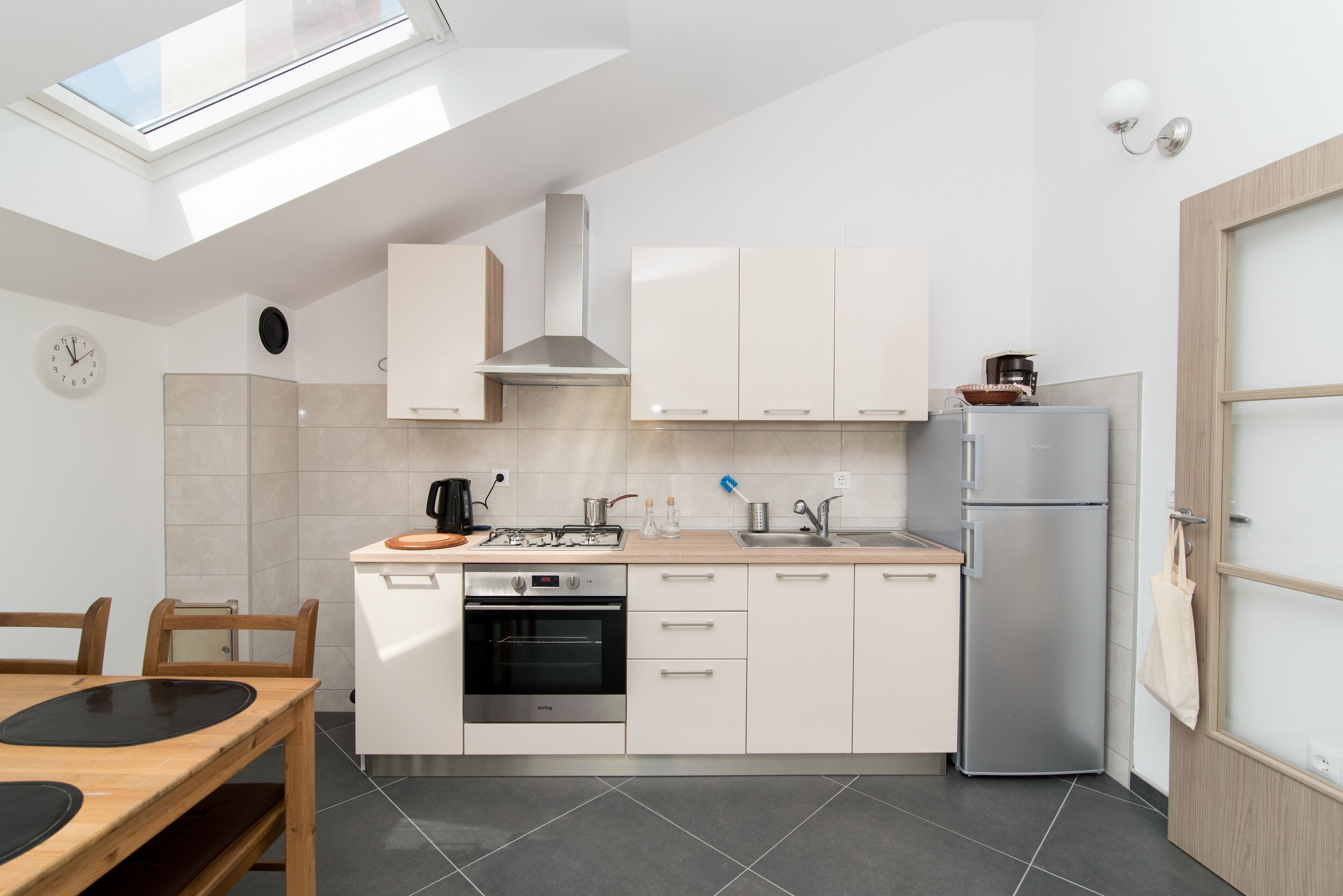 A modern kitchen with a skylight, a built-in oven, and a refrigerator.