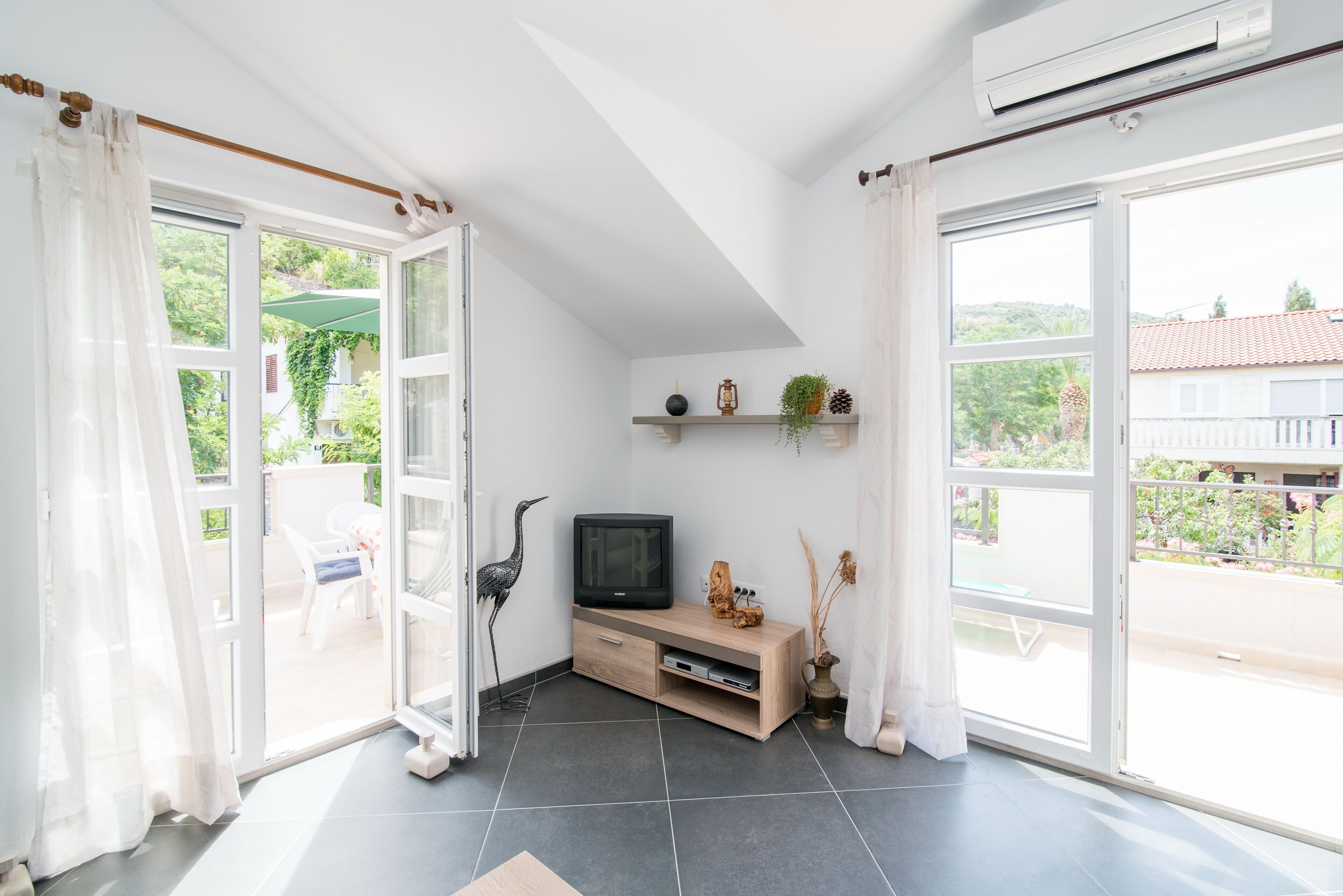 A bright living room with a TV, shelves with plants, and a view of the outdoors.