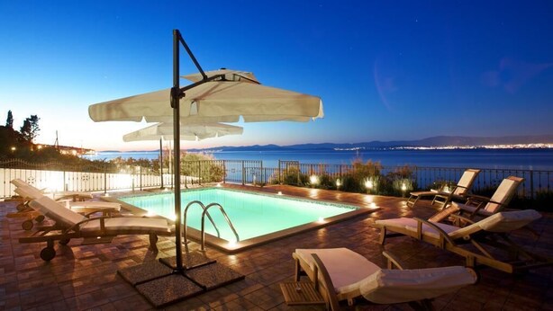 Une piscine entourée d’une clôture, dotée de chaises longues et de parasols, et offrant une vue sur une étendue d’eau.