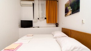 Un dormitorio con cama, televisor, un cuadro y ventana con cortinas.