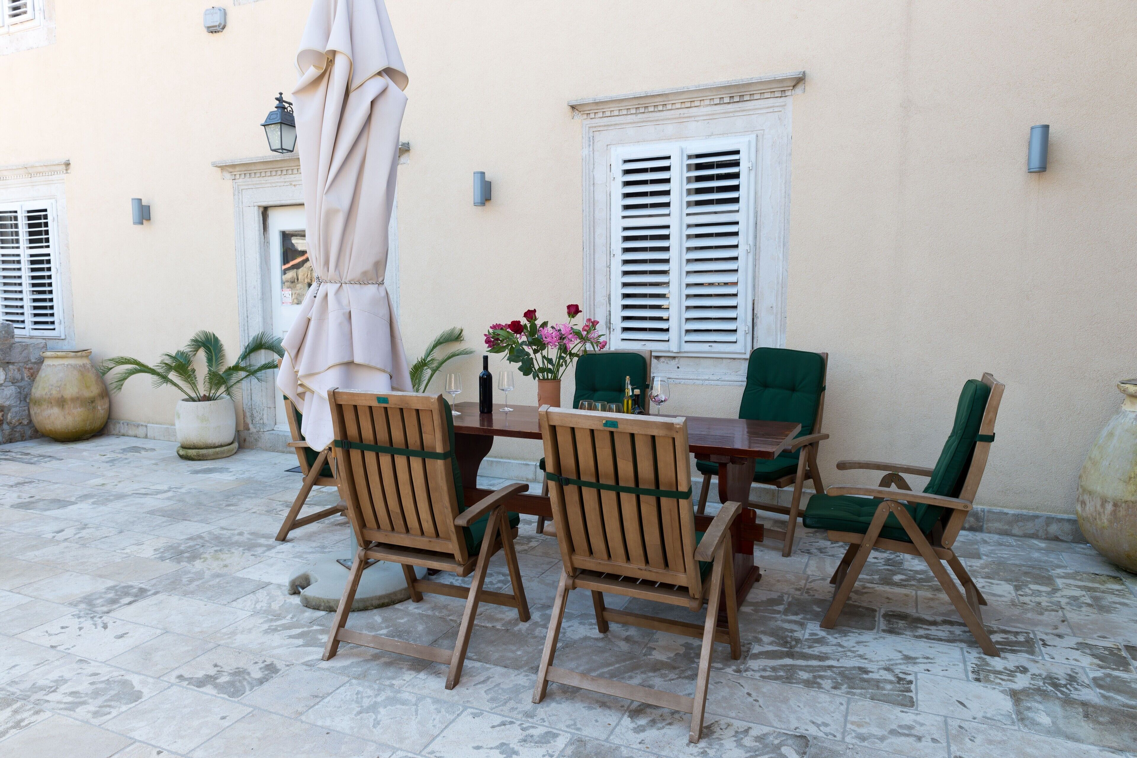 An outdoor patio with a table and chairs, a potted plant, and a large vase with flowers.