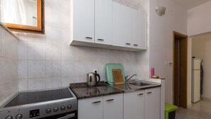 A kitchen with white cabinets, a stove, a sink, and a green trash bin. - Apartments Kisic - Two-Bedroom Apartment with Terrace(prizemlje) (Mlini)