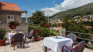 A terrace with a table and chairs, potted plants, and a view of a town and hills. - Guest House Raguz - Double room - 5 (Dubrovnik)
