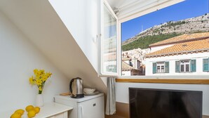 A small kitchenette with a refrigerator, a kettle, and a bowl on the counter. There is a TV on a stand and a window with a view of a hillside. - Guest House Lumin - Deluxe Single Room with City View (Fourth Floor) (BR5) (Dubrovnik)