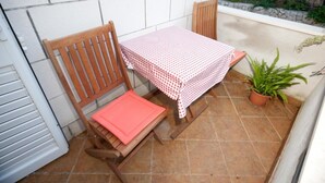 A small patio area with a wooden chair and table, a potted plant, and a stone wall in the background. - Apartments Briest - Studio Apartment with Balcony (Dubrovnik)