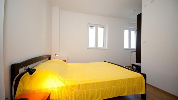 A bedroom with a bed, a nightstand, a lamp, and a window. - Apartments Briest - Studio Apartment with Balcony (Dubrovnik)