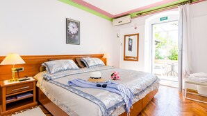 Hotellihuone, jossa on puinen sänky, yöpöytä lampun kanssa ja lasiovesta avautuva näkymä ulos.
