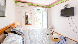 Hotellihuone, jossa on sänky, seinälle asennettu televisio, ikkuna, jossa on hätäuloskäyntiä osoittava opaste, ja ovi, joka johtaa ulos.