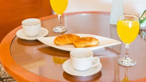 Aamiaispöytä, jossa on croissantteja, kaksi kuppia kahvia ja kaksi lasillista appelsiinimehua pyöreällä pöydällä.