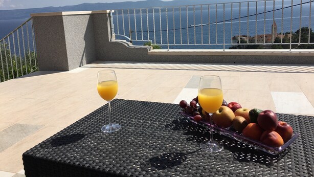 A table with two glasses of orange juice and a fruit tray on a balcony overlooking a coastal view with mountains in the distance. - Apartments Eastern Paradise- Comfort One Bedroom Apartment with Terrace and Sea View (Bol)