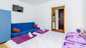 A bedroom with a blue sofa, a bed with purple bedding, and a TV mounted on the wall. - Apartments & Rooms Mihajica- Comfort Studio Apartment with Balcony and Sea View (Cavtat)
