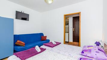Ein Schlafzimmer mit einem blauen Sofa, einem Bett mit violetter Bettwäsche und einem an der Wand befestigten Fernseher.
