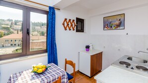A compact kitchen with a dining area, a small refrigerator, and a window with a view of buildings. - Apartments & Rooms Mihajica- Comfort Studio Apartment with Balcony and Sea View (Cavtat)