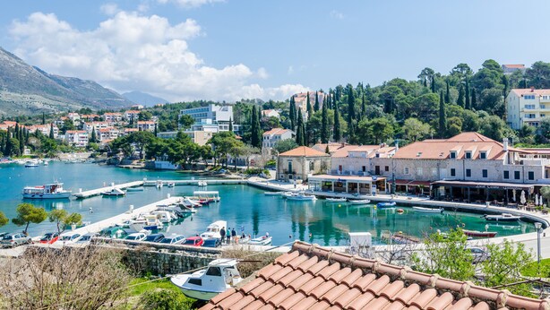 A marina with boats docked, a waterfront building with a terrace, and a mountainous backdrop. - Apartments & Rooms Mihajica- Comfort Studio Apartment with Balcony and Sea View (Cavtat)