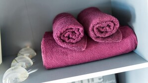 Ein Regal mit aufgerollten violetten Handtüchern und einem klaren Glasobjekt.