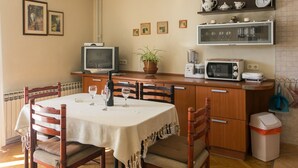 Un comedor con una mesa dispuesta para dos, un televisor, un microondas y un estante con utensilios de cocina.