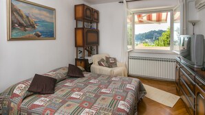 Un dormitorio con cama, televisión, ventana con vistas y un cuadro en la pared.