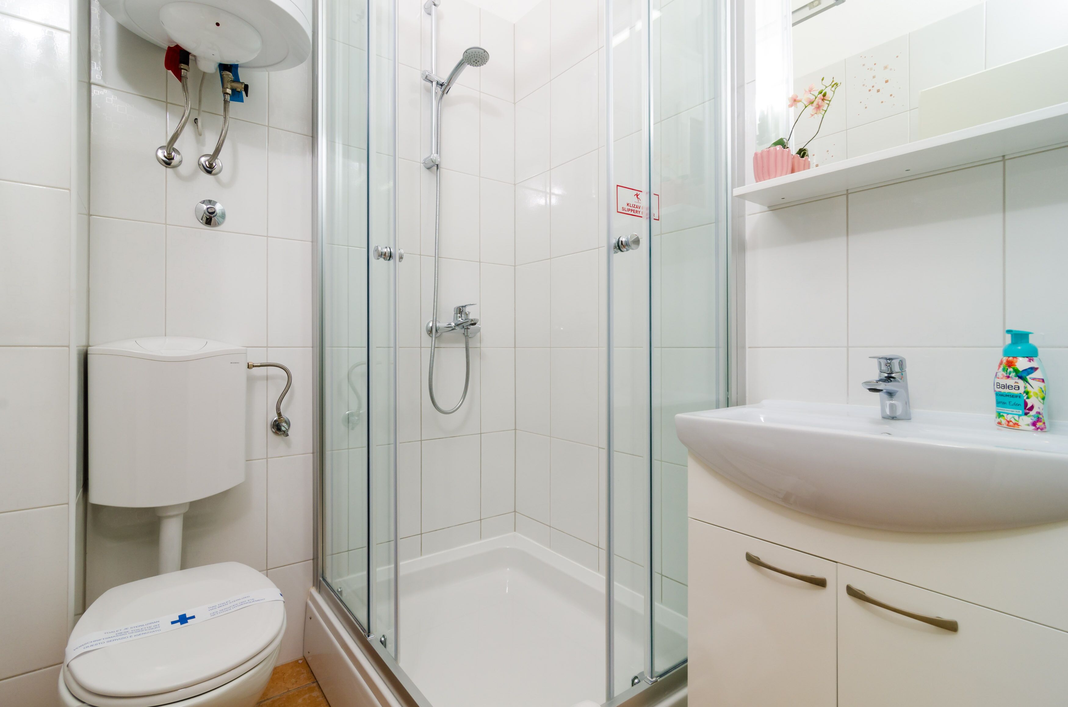 A modern bathroom with a glass shower enclosure, a toilet, and a sink with a mirror above.